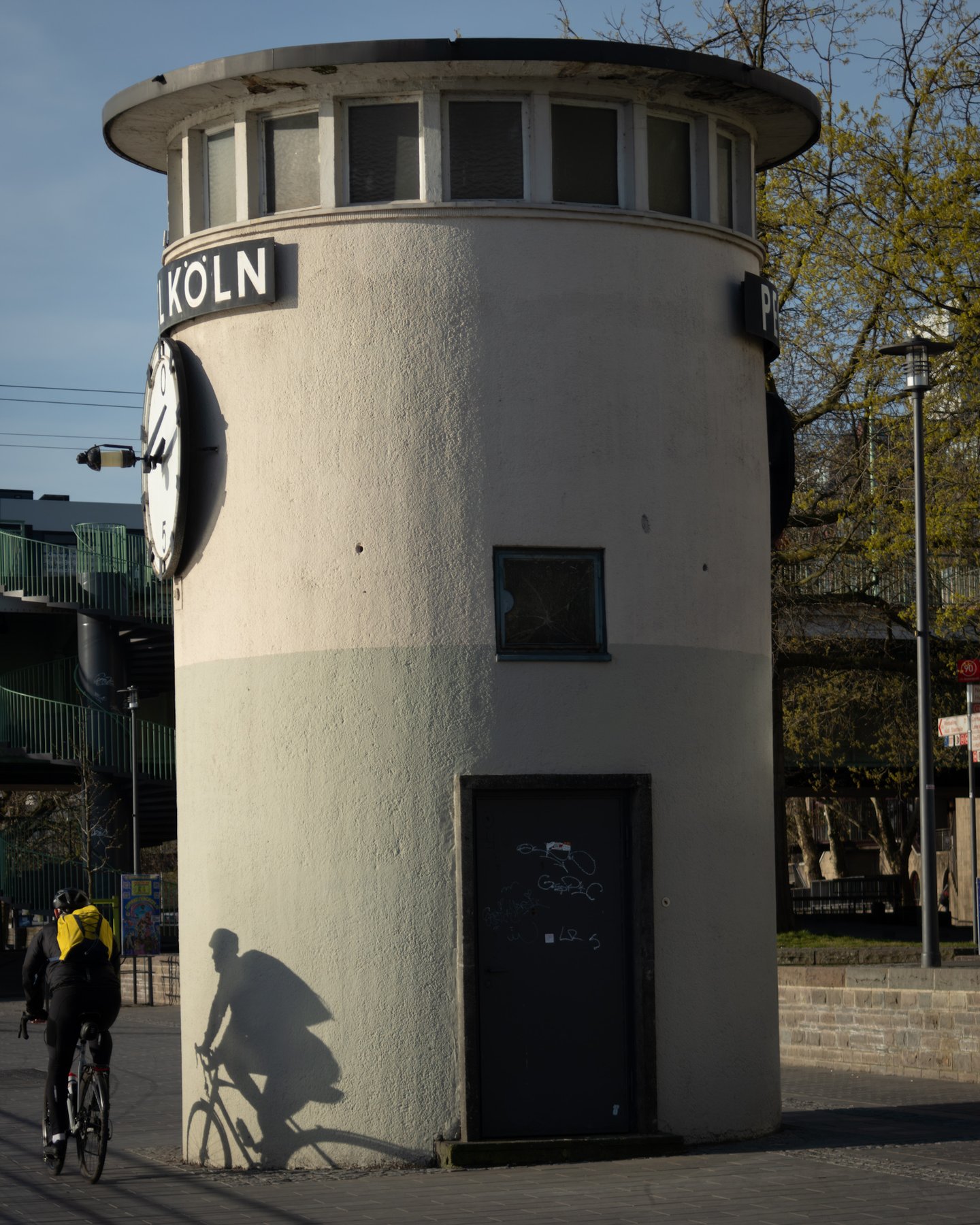 Cyclist passing a rounded clock tower marked KOELN near the main station